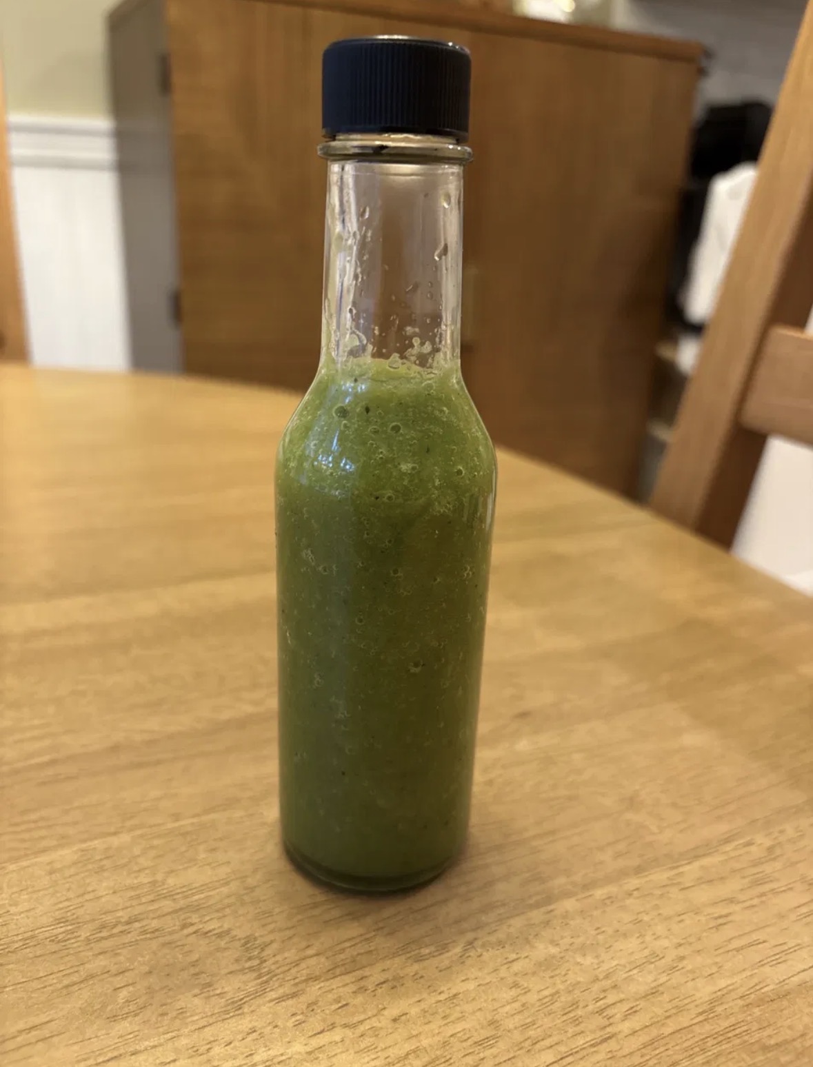 A bottle of vibrant green fermented jalafuego hot sauce on a wooden table